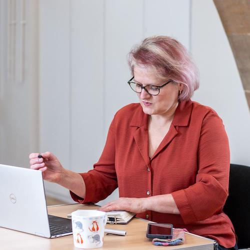 Anne Barrett is sitting at a desk, looking down at a notebook she is writing in.